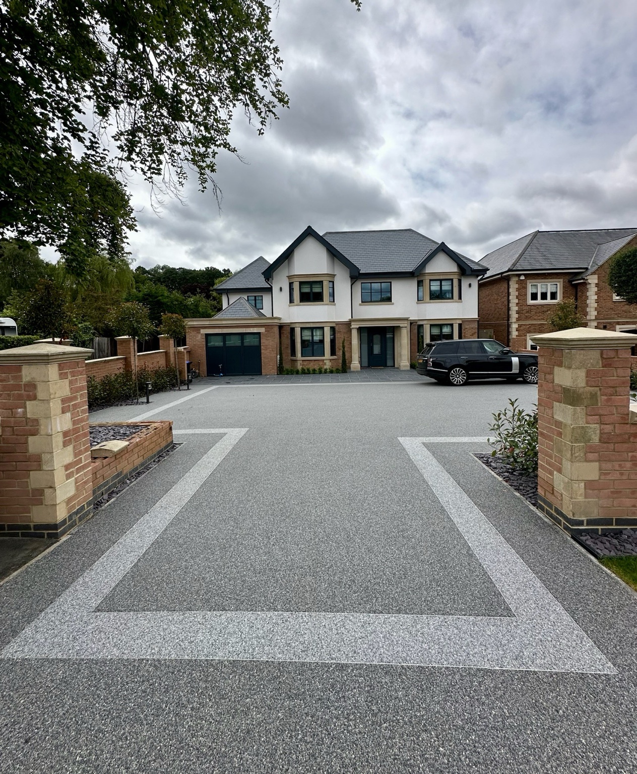 Grey resin driveway with a light contrasting border between brick pillars