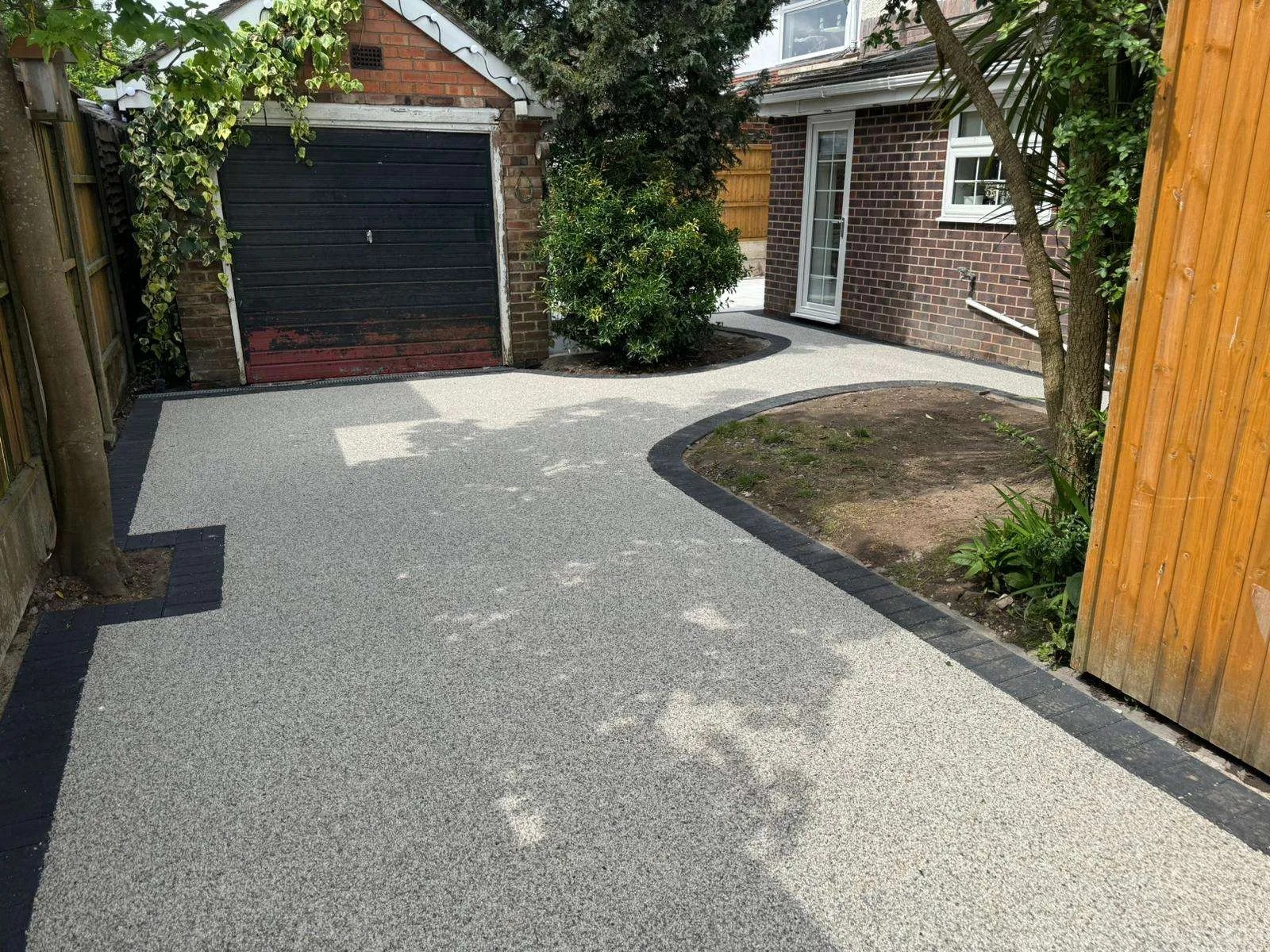 Grey resin surface with curved dark edging beside a garage