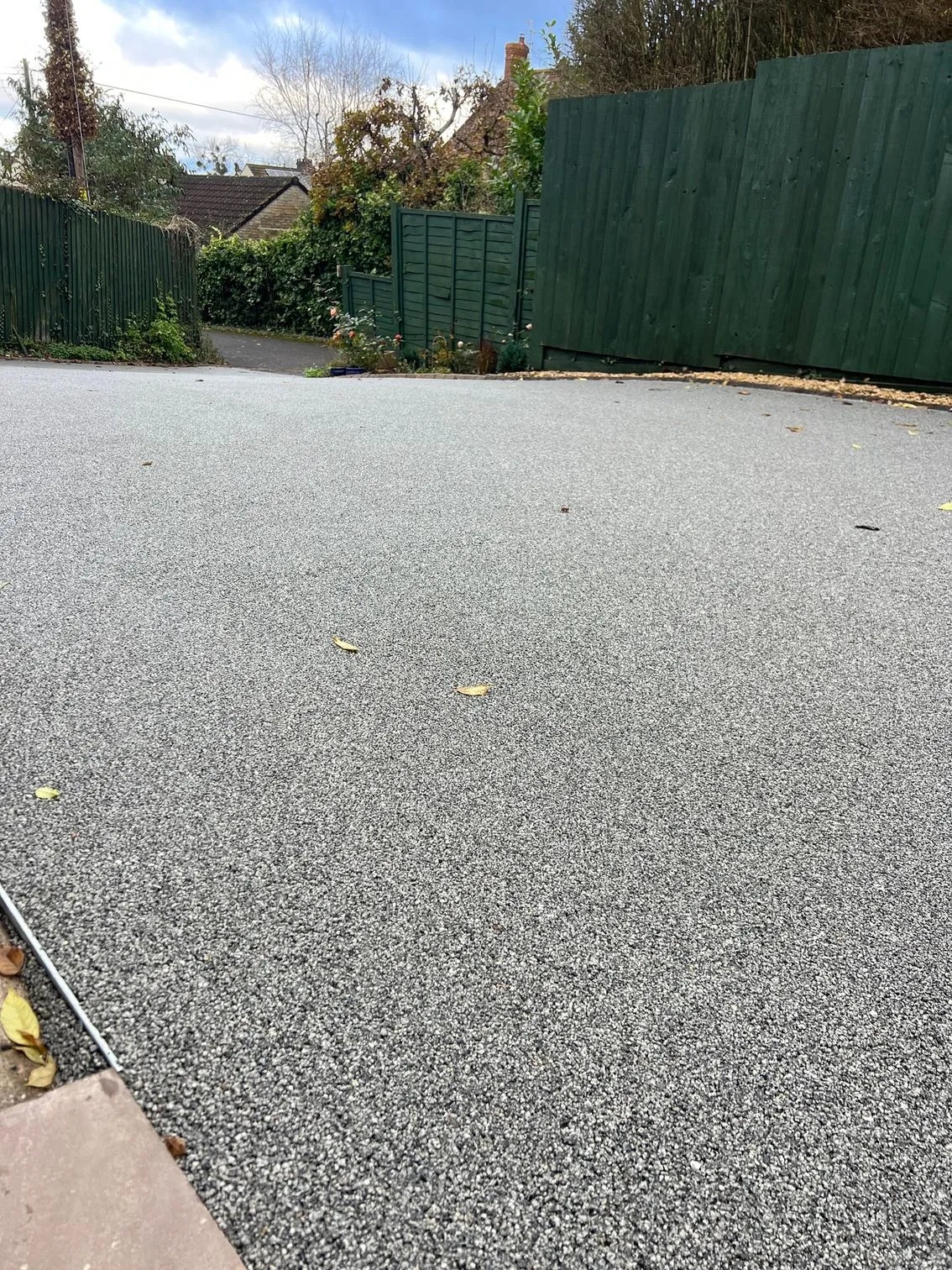 Light grey finished driveway surface beside a green fence